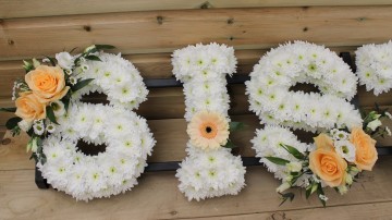Sister funeral tribute foliage edge based in white chrysanthemum with peach rose sprays
